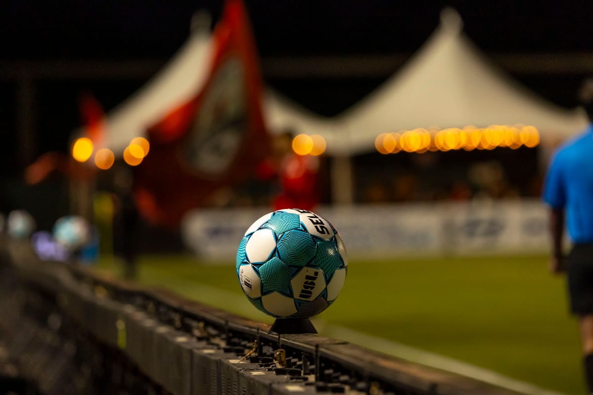 A soccer ball on the pitch with cheering fans in a stadium